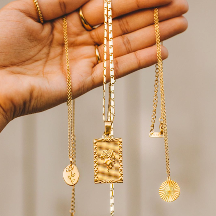 An image of a person dangling three different gold necklaces of different lengths showing how to layer necklaces.