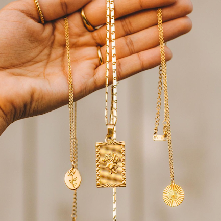 An image of a person dangling three different gold necklaces of different lengths showing how to layer necklaces. 
