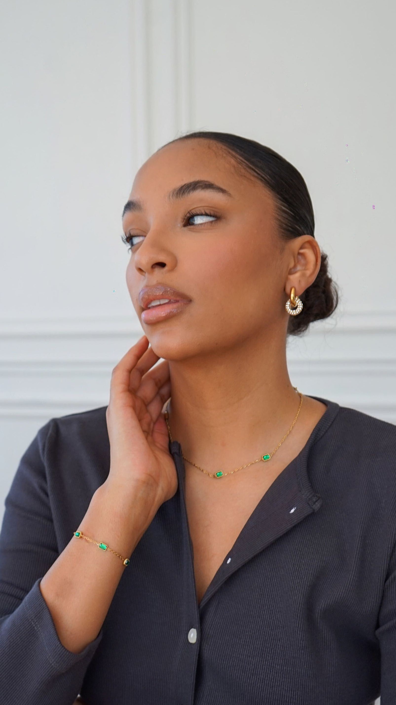 Woman wearing a dark gray button-up shirt against a white paneled wall.